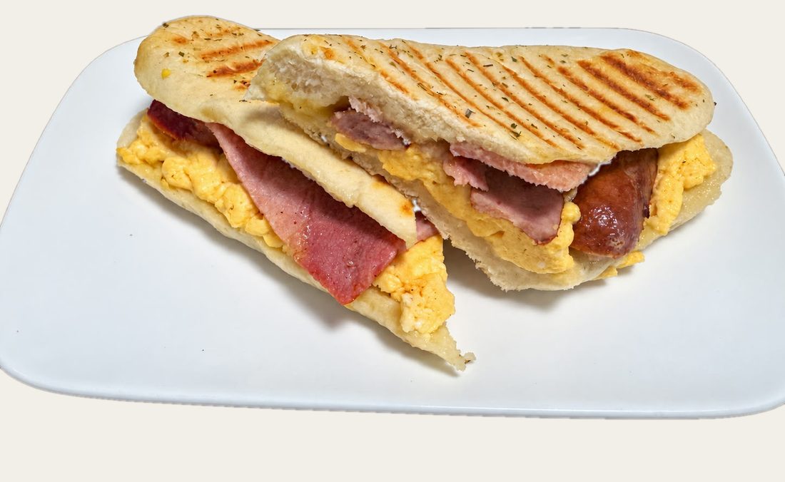 A breakfast panini with bacon, sausage, scrambled egg and cheese